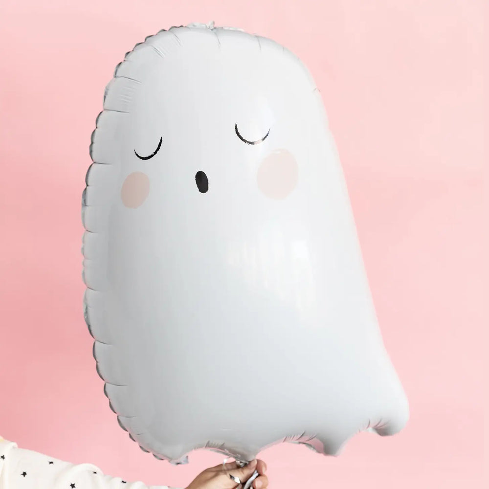 White ghost Mylar balloon being held by a woman with a white blouse with black stars photographed on a pink backdrop.