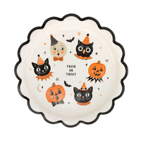 Round cream plate with printed graphics including two Jack-O Lanterns, two cats, owl, moon, flying bats and stars with a black scalloped edge and “ trick or treat “ written in center of plate.

