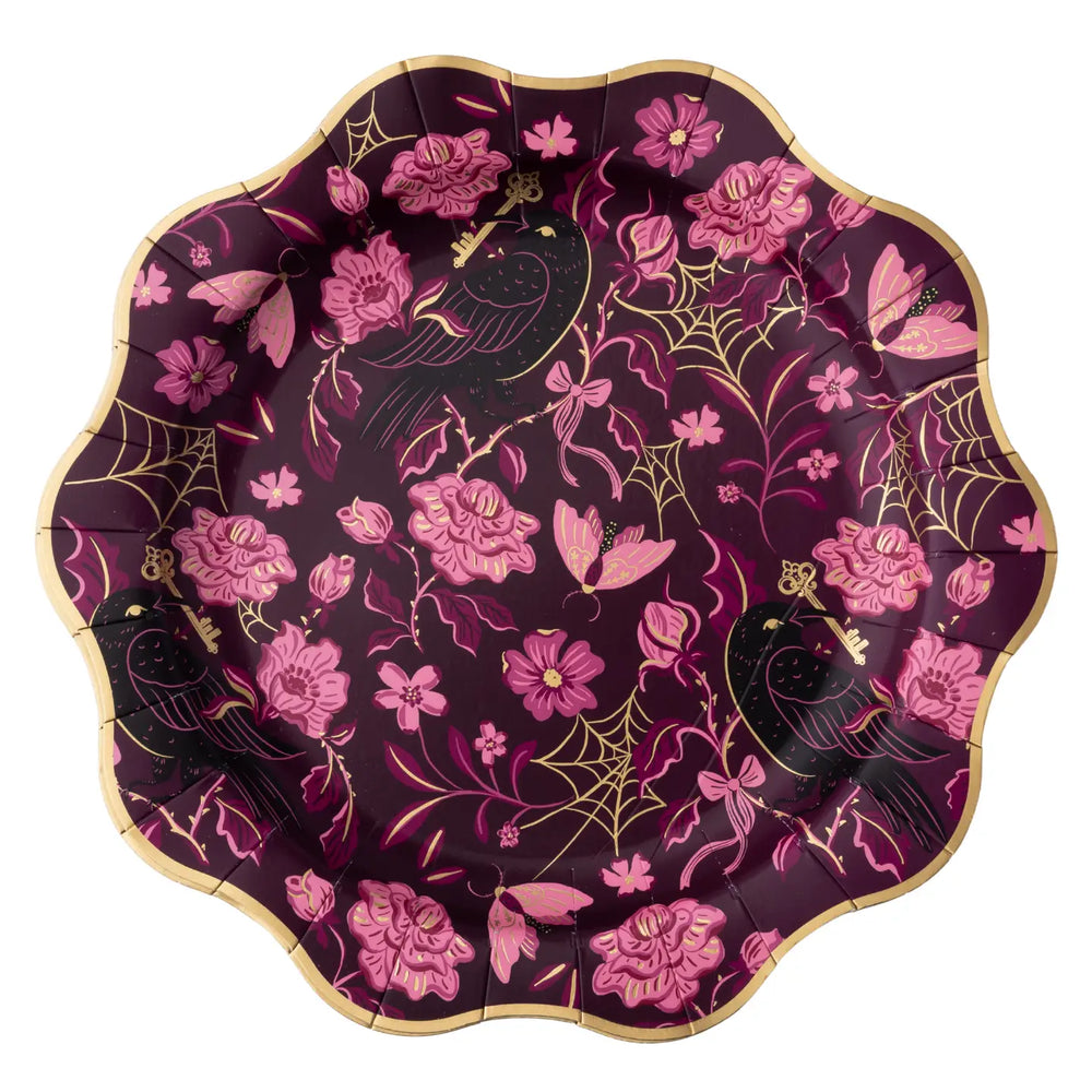A scalloped paper plate with a gothic design featuring pink flowers, black ravens, gold web motifs, and gold keys on a dark purple background.
