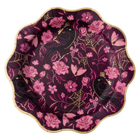 A scalloped paper plate with a gothic design featuring pink flowers, black ravens, gold web motifs, and gold keys on a dark purple background.